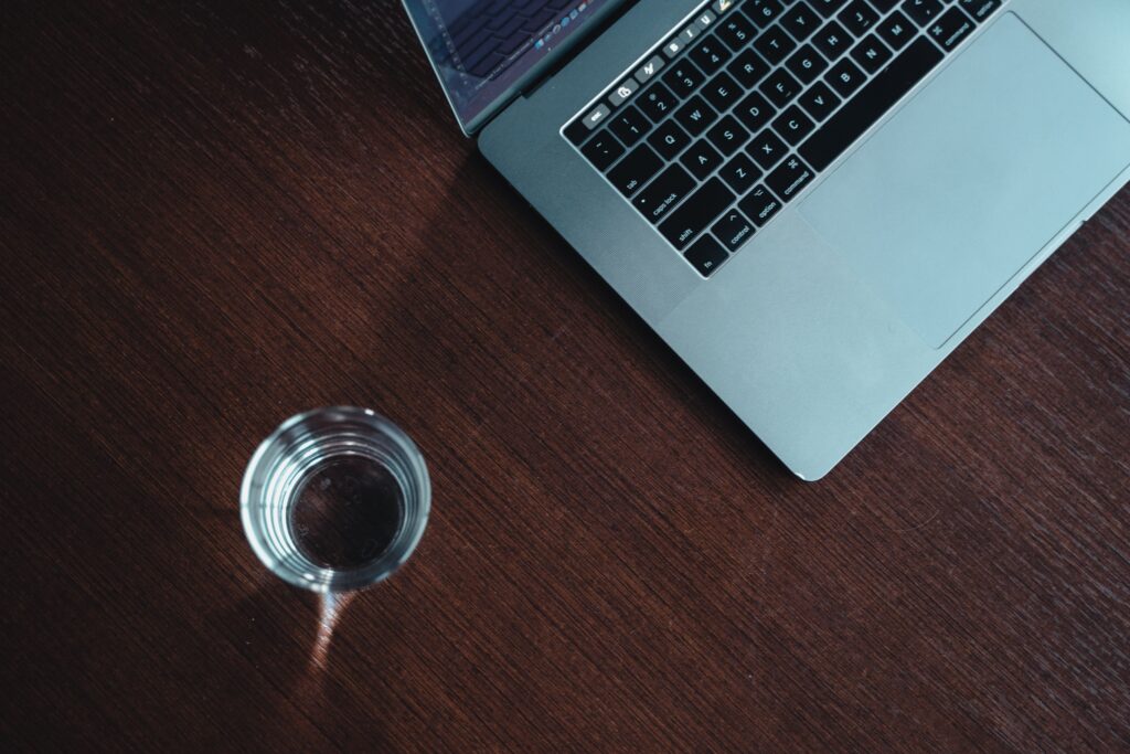 A modern workspace featuring a laptop and a glass of water on a wooden desk.